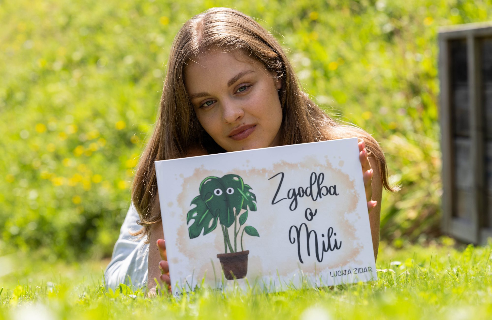 Dekle leži na travi in drži knjigo Zgodba o Mili